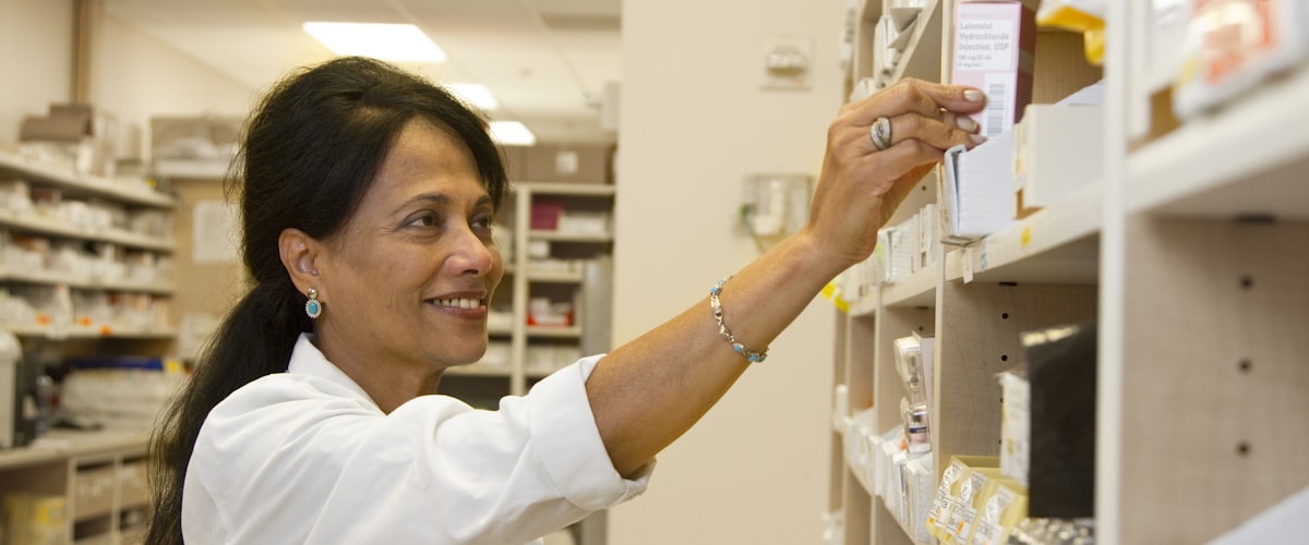 Pharmacist preparing prescription medicines at the dispensary shelves of Barons Court Pharmacy, London W6